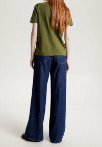 Olivgrön bomullströja med korta ärmar, kombinerad med vida mörkblå denimjeans som har bakfickor och en avslappnad passform.