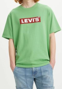 Zelené bavlněné tričko s volným střihem, s červeným obdélníkovým logem Levi's přes hruď. Krátké rukávy a design s kulatým výstřihem.
