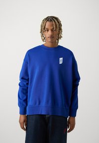 Felpa blu royal con texture a coste, colletto rotondo e logo ricamato sul petto. Vestibilità comoda e maniche lunghe.