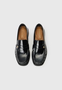 Mocassins de cabedal preto com um acabamento suave, apresentando um acabamento costurado, uma faixa decorativa e uma palmilha em tom de caramelo com letras da marca.