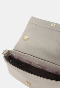Sac en cuir gris clair avec une surface texturée, quincaillerie circulaire dorée et une doublure intérieure violette comportant un motif de logo subtil.