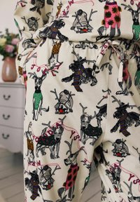 Ropa de lounge con una tela crema que presenta patrones de perros coloridos, incluyendo renos, bufandas y textos de temática navideña en rosa y verde.