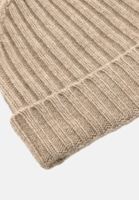 Beige stickad mössa med ribbat mönster, mjukt ullmaterial och en vikt kantdetalj. Designen är enkel och funktionell.