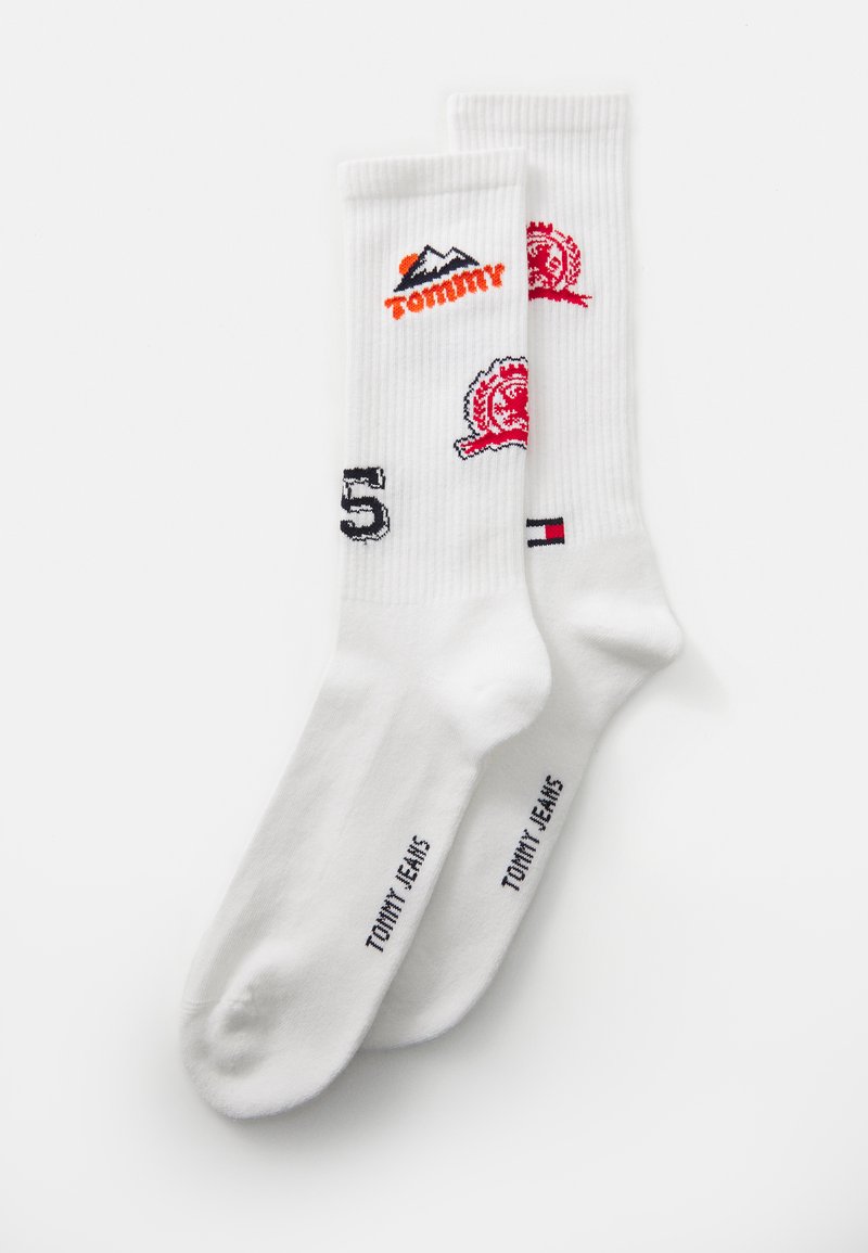 Weiße Crew-Socken mit Tommy Jeans-Logos, roten und schwarzen gestickten Designs sowie der Zahl 85 auf einem schlichten weißen Hintergrund.