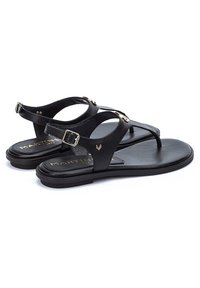 Sandales en cuir noir avec un design à lanières, éléments en métal doré, semelle plate et léger soutien de la voûte plantaire. Nom de la marque visible sur la semelle intérieure.