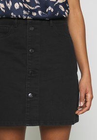 Jupe en denim noir avec une coupe ajustée, dotée de cinq boutons sur le devant et de détails de couture subtils.