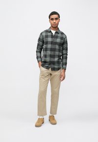 Plaid shirt in dark and light green, button-up design, paired with beige pants and tan sneakers. Minimalist style, smooth texture.