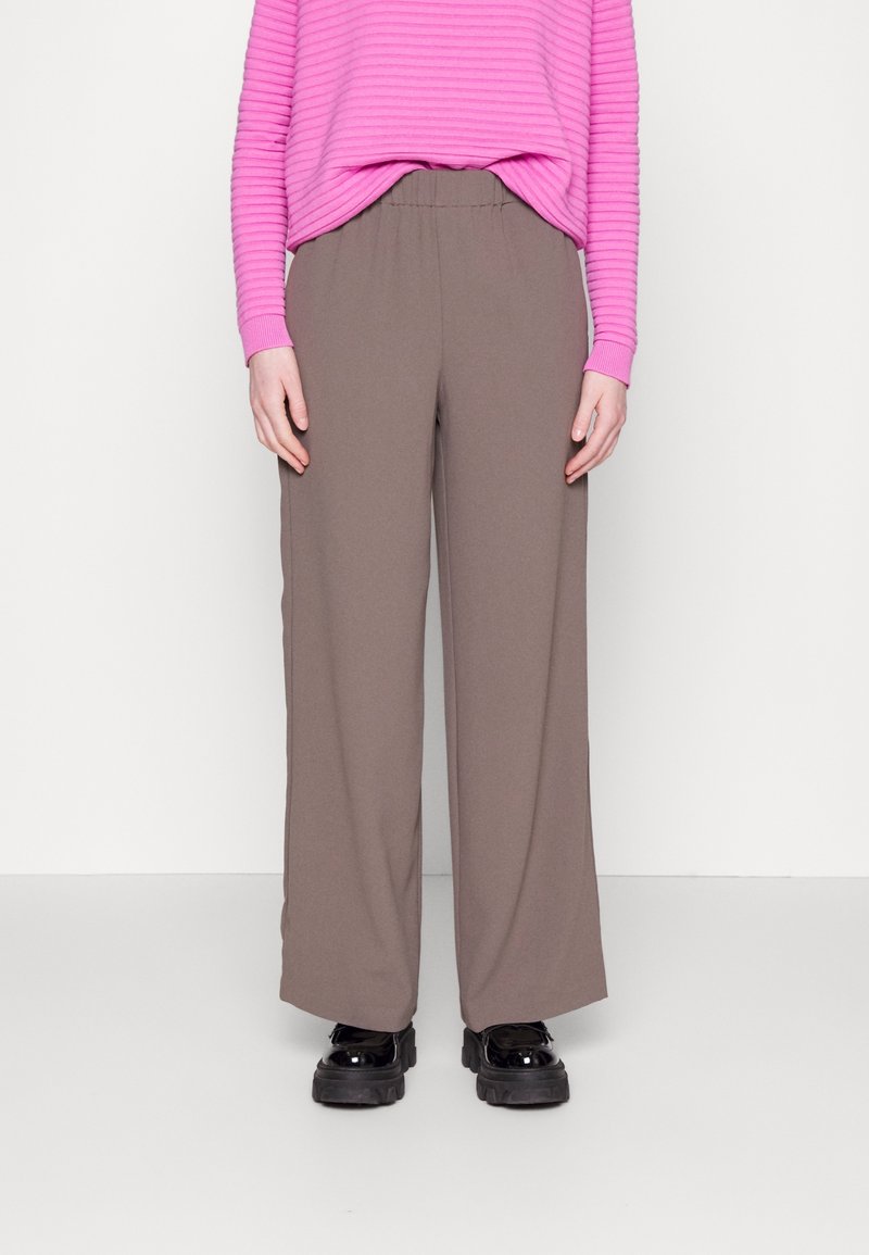 Breda ben, bruna byxor gjorda av mjukt tyg, i kombination med en randig tröja i rosa och kraftiga svarta skor. Enkelt mönster med elastisk midja.