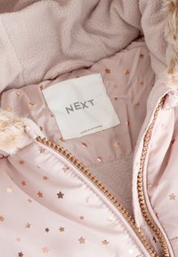 Unutrašnjost ružičaste podstavljene jakne s mekanim flisnim uloškom, uzorci zlatnih zvjezdica i sjajni zlatni patentni zatvarač. Oznaka "NEXT", proizvedeno u Mjanmaru.