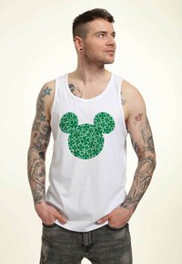 Top sin mangas blanco con una silueta de Mickey Mouse verde y foliosa en la parte delantera. La tela es suave y el diseño es gráfico y audaz.