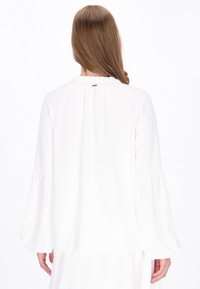 Weiße Bluse mit langen, ausgestellten Ärmeln und gerafftem Ausschnitt. Glatte Textur mit lockerer Passform, die einen dezenten Fall zeigt.