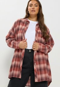 Czerwona i biała koszula w kratę z guzikami, z długimi rękawami, w lekkim oversize'owym kroju, połączona z białym T-shirtem i czarnymi spodniami o wysokim stanie.