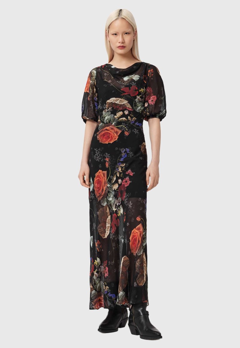 Vestido largo con mangas cortas abullonadas, tela negra transparente adornada con estampados florales vibrantes en rojo, amarillo y púrpura, combinado con botines negros hasta el tobillo.