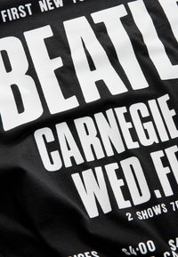 Black fabric featuring bold white text. The design includes event details and a prominent mention of "BEATLES" with a textured appearance.
