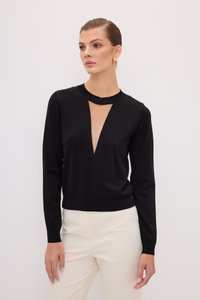 Schwarzer Pullover mit langen Ärmeln, tiefem V-Ausschnitt und strukturiertem Stoff. Der untere Saum hat ein geripptes Strickdetail. Getragen mit cremefarbenen Hosen.