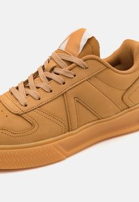 Braune Sneakers aus glattem synthetischen Material mit strukturierten Akzenten, flachen Schnürsenkeln, einem gepolsterten Innenraum und einer Gummisohle mit einem gemusterten Profil.