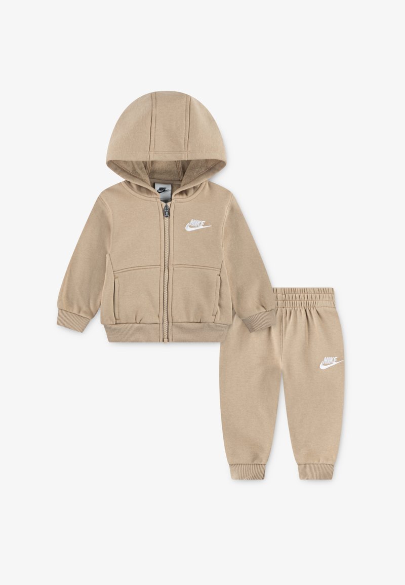 Fato de treino em algodão bege, com uma hoodie com fecho éclair, capuz e bolsos frontais, combinado com calças de treino correspondentes, ambos com um logótipo branco.