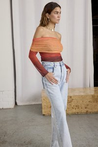 Off-the-shoulder topp i gradient oransje og rød gjennomsiktig stoff med lange tettsittende ermer, sammen med høyt liv lyseblå denimjeans.