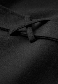 Czarna wełniana tkanina o miękkiej fakturze, z podwójnym węzłem jako detal. Gładka powierzchnia z subtelnymi wariacjami głębokości i cienia.