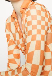 Il top a maniche lunghe presenta un motivo a scacchi arancione e crema, design con colletto, in un tessuto morbido e elastico, silhouette aderente e texture liscia.