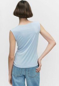 Ljusblå ärmlös topp gjord av mjukt tyg; har en båtformad halsringning och en figurnära design, med jämn textur och subtil lyster.