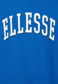 Tejido azul con grandes letras blancas, en negrita y mayúsculas, que dicen "ELLESSE" en un diseño arqueado.