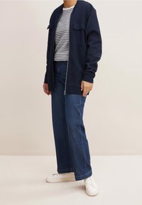 Marinblå bomberjacka med två framfickor, randig skjorta under, vida blå jeans och vita sneakers. Mjukt tyg och avslappnad passform.