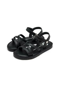 Sandalias negras con múltiples tiras entrecruzadas, suela plana y una pequeña hebilla plateada en la correa del tobillo. Textura de cuero suave.