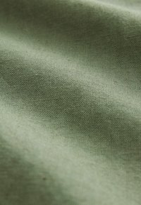 Tkanina z teksturo v mehki olivno zeleni barvi, fino tkanje z gladko površino. V materialu so subtilne razlike v odtenkih.