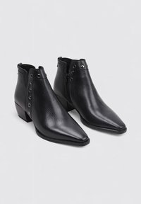 Botas de tobillo de cuero negro con puntera puntiaguda, acabado texturizado y cremallera interior. Presentan herrajes plateados con remaches decorativos a lo largo del costado.