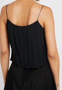 Débardeur plissé noir avec des bretelles fines et une coupe ample. Le tissu est doux avec une texture subtile, tombant juste en dessous de la taille.