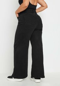 Mustat farkut leveillä lahkeilla, joissa on joustava vyötärö, sivutaskut ja takataskut. Teksturoitu kangas, jossa on hieno kiilto.