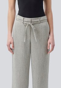 Gray and white herringbone patterned pants with a relaxed fit, waist tie, and textured fabric. Front view shows hands resting on fabric.