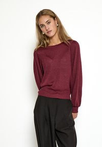 Bordowy sweter z dzianiny z długimi, luźnymi rękawami i ściągaczem u dołu. Połączony z czarnymi spodniami o wysokim stanie. Prosty, elegancki design.