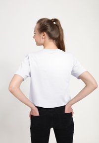 Bílý bavlněný tričko s krátkými rukávy, kulatým výstřihem a volnějším střihem, spárované s černými slim fit džíny, zobrazené zezadu.