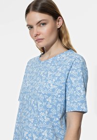 T-shirt à manches courtes bleu clair avec un motif floral blanc. Conception à col rond avec une texture douce et une coupe décontractée.