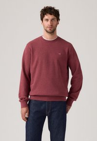 Bordeaux sweatshirt van textuurstof, met een ronde halslijn en ribgebreide mouwen, voorzien van een klein logo op de borst. Gecombineerd met donkere denim.