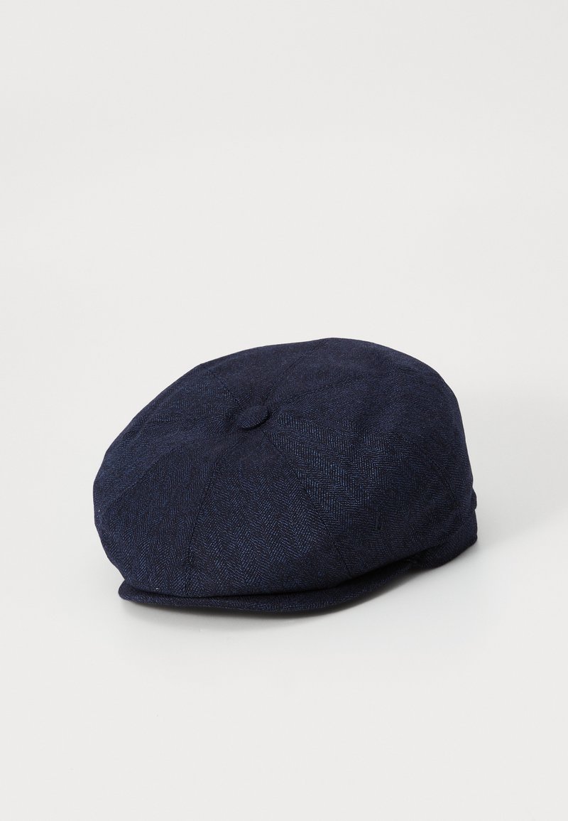 Dark blue herringbone patterned flat cap with a small button on top, resting on a white surface.