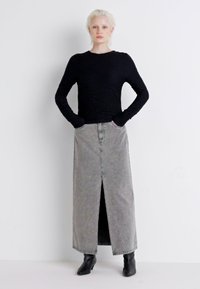 Svart teksturert langermet topp kombinert med en høytlivd grå denim maxiskjørt med en frontsplitt, båret med svarte ankelboots.