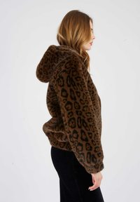 Brązowa bluza z futra syntetycznego w wzór panterki, z szerokim dekoltem i bocznymi kieszeniami, w połączeniu z czarnymi spodniami z kordurowej tkaniny.