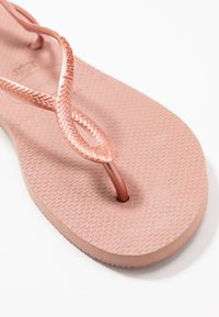 Chinelo rosa de borracha com sola texturizada e tiras trançadas. As tiras são de cor rosa metálico, apresentando um acabamento suave e extremidades arredondadas.