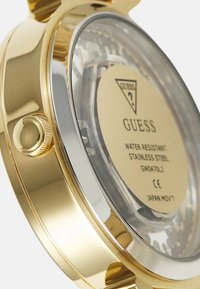 Orologio con cassa in acciaio inox dorato e fondo trasparente, dotato di un accento argento e una corona strutturata per regolare le impostazioni dell'ora.