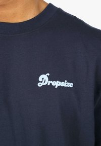 Morska pamučna majica s okruglim izrezom koja ima svijetloplavi "Dropsize" logotip na grudima, glatku teksturu i rebrasti izrez.