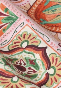 Tissu coloré avec des motifs floraux et géométriques élaborés dans des tons verts, orange, rouge et beige, montrant la texture et les plis.