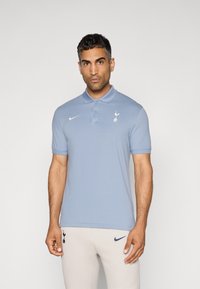 Lyseblå polo med krave, korte ærmer, Nike-logo i hvid og Tottenham Hotspur-emblemet på venstre bryst. Glat overflade.