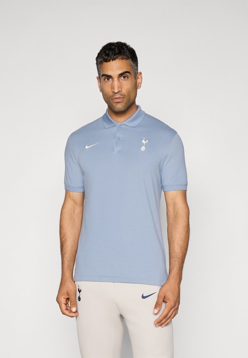 Lyseblå polo med krave, korte ærmer, Nike-logo i hvid og Tottenham Hotspur-emblemet på venstre bryst. Glat overflade.