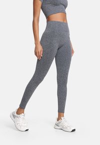 Szare legginsy do ćwiczeń z wysokim pasem i fakturowaną tkaniną, zestawione z białymi butami sportowymi z szarymi akcentami.