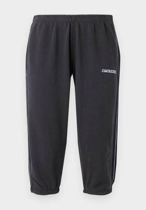 Pantaloni de jogging negri cu talie și glezne elastice, dungi laterale albe și mic logo alb pe partea superioară a coapsei.