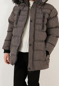 Tummanharmaa keskipitkän pituinen toppatakki vaakasuorin tikatuin saumin, jossa on karvareunuksella varustettu huppu, kaksisuuntaiset vetoketjutaskut ja resorireunaiset hihansuut.