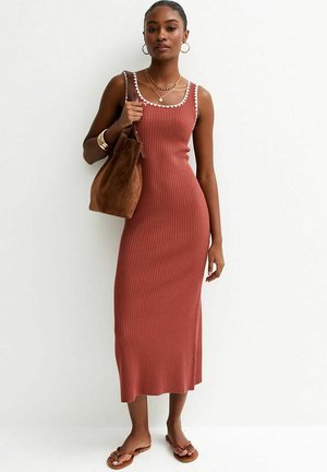 Femme portant une robe sans manches côtelée couleur rouille avec des bordures blanches, portant un sac à bandoulière en daim marron, des sandales et des bijoux.